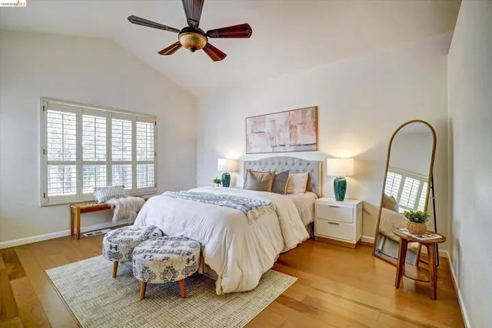Vaulted ceiling bedroom featuring plantation shutters, wood-finish flooring, and a ceiling fan