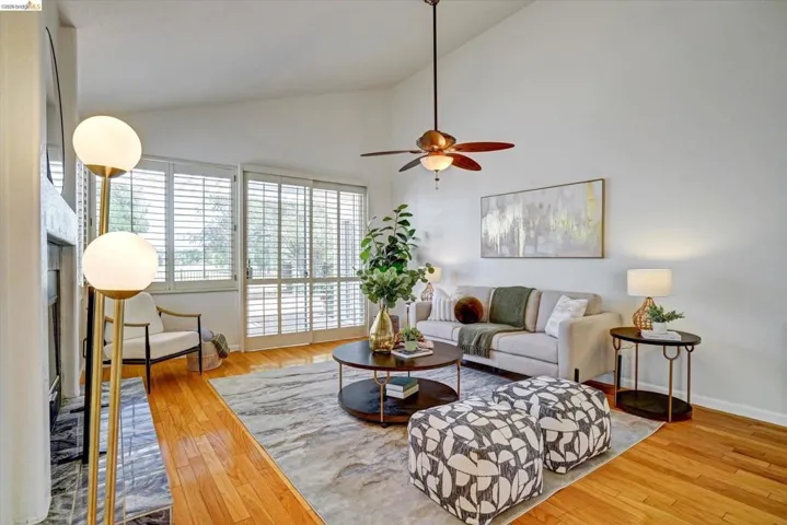 Living area featuring vaulted ceilings, wood-finish flooring, a ceiling fan, and sliding glass doors with plantation shutters