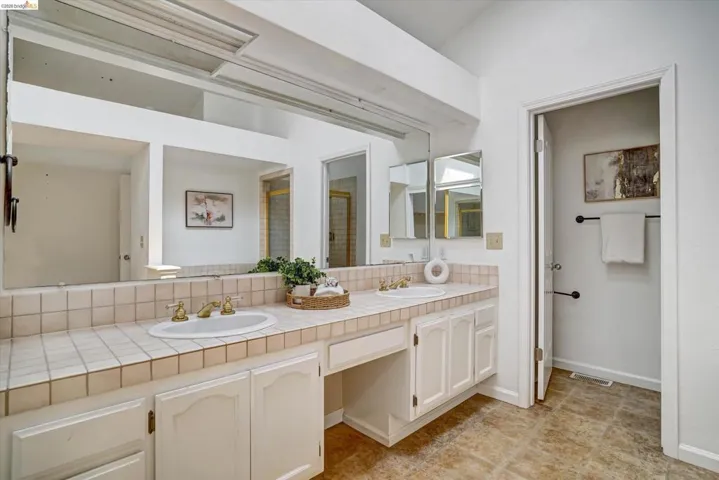 Dual vanity with integrated sinks, brass-finish faucets, tiled countertop, and ample under-sink storage