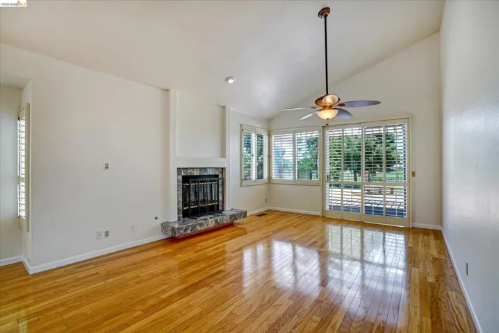 Unfurnished living room with vaulted ceiling, light wood finished floors, a ceiling fan, and a fireplace