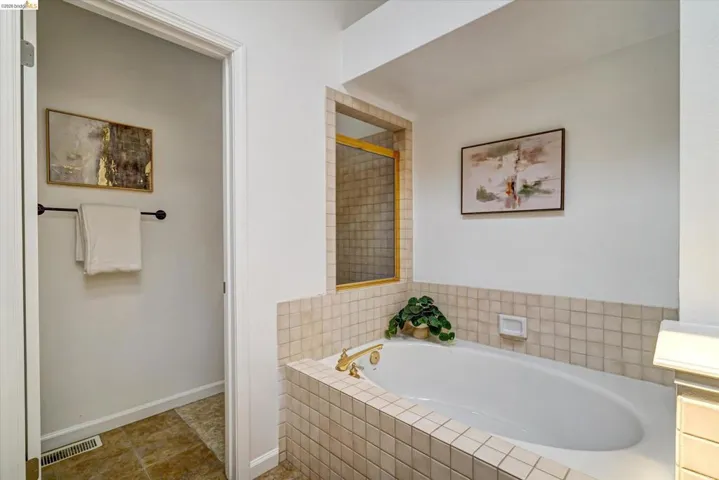 Built-in soaking tub with gold-tone fixtures, surrounded by neutral-toned square tile