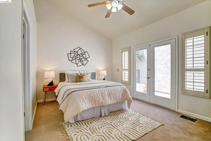 Vaulted ceiling with a ceiling fan, dual French doors, two windows with plantation shutters, and carpeted flooring