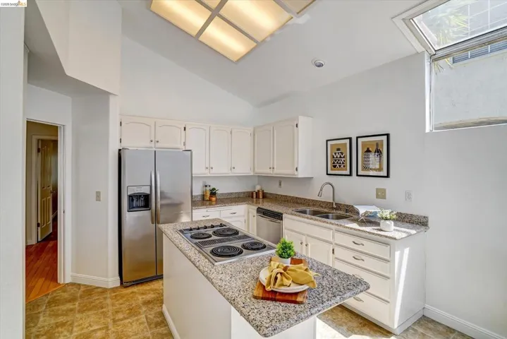 Kitchen featuring a vaulted ceiling with a large skylight, an additional window, white cabinetry, and granite countertops