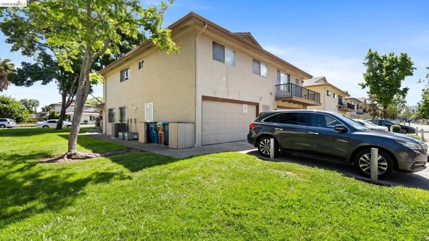 View of side of home with an attached garage, a lawn, stucco siding, and a balcony