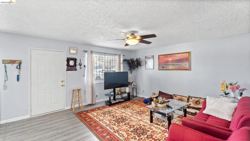 Living room with a ceiling fan, light wood-style floors, and a textured ceiling