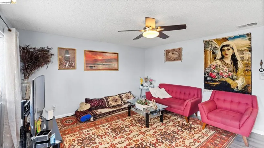 Living room featuring a ceiling fan, a textured ceiling, and wood finished floors