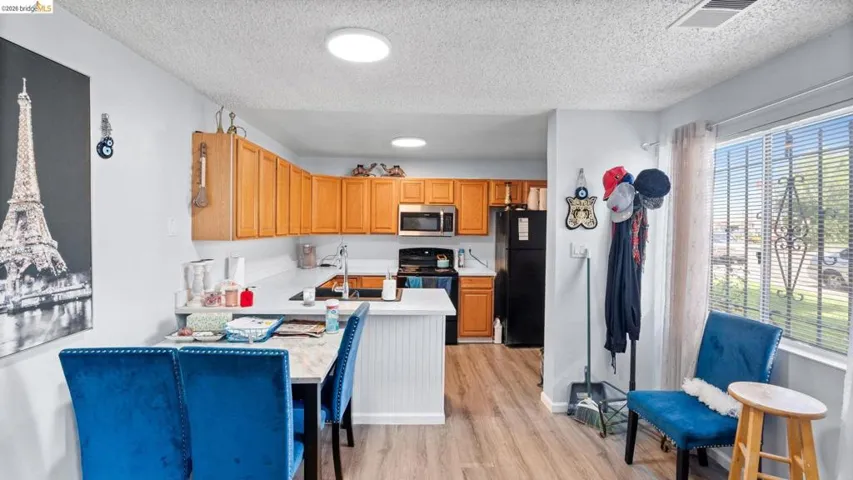 Kitchen featuring light countertops, black appliances, light wood-style floors, a textured ceiling, and wood finish cabinetry