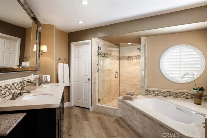 The primary bathroom is elegantly upgraded with a Restoration Hardware vanity, Crema Marfil marble, tile finishes, and a shower with a tumbled marble enclosure, tile inlay, and seamless glass door.