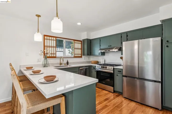 Kitchen featuring green cabinetry, a peninsula, stainless steel appliances, and a kitchen breakfast bar