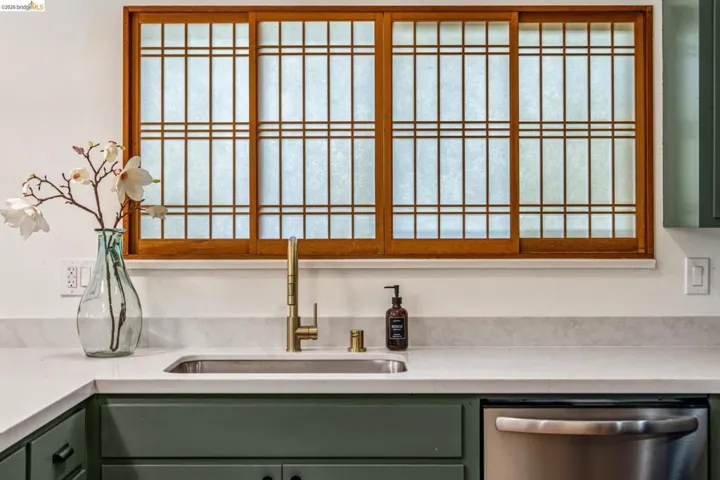 Kitchen view of green cabinets, dishwasher, and light stone countertops