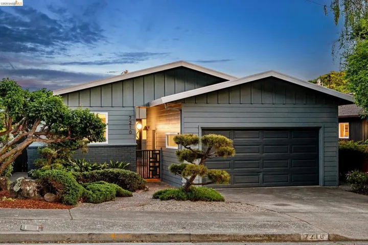 Ranch-style house with a garage, concrete driveway, and board and batten siding. Digitally altered to remove power line.
