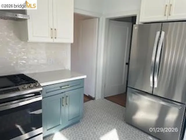Kitchen with stainless steel appliances, ventilation hood, light countertops, decorative backsplash, and two tone cabinets