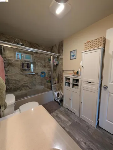 Full bathroom with dark wood-style flooring, enclosed tub / shower combo, and vanity
