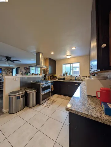 Kitchen with range with two ovens, dark stone counters, island exhaust hood, a ceiling fan, and light tile patterned floors