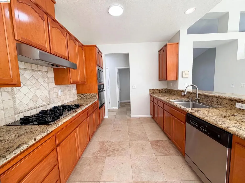 Kitchen with light stone countertops, stainless steel appliances, and wood finish cabinets