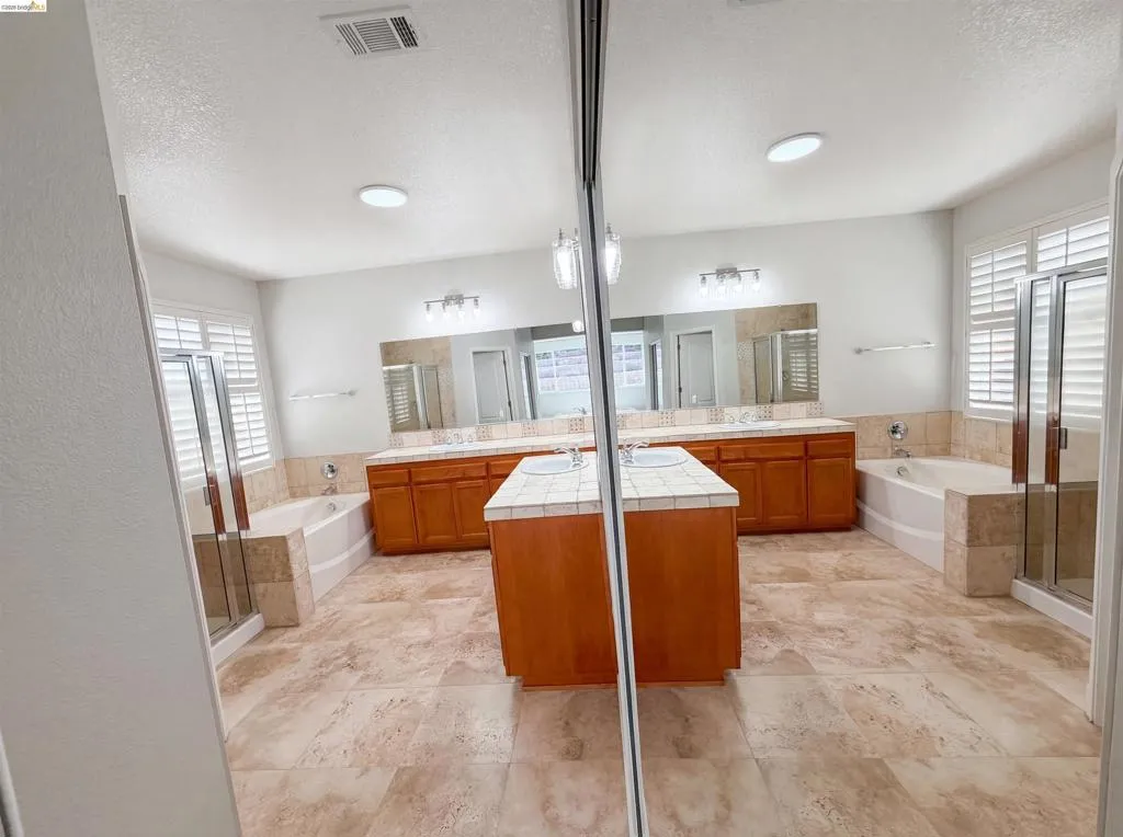 Bathroom featuring a garden tub, a stall shower, two vanities, and a textured ceiling