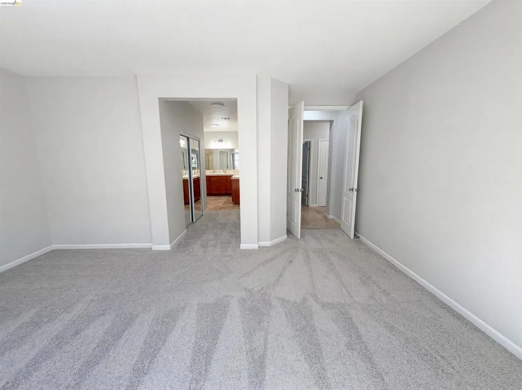 Empty room with light colored carpet and baseboards