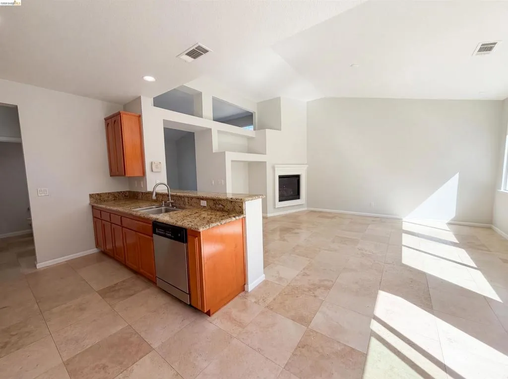 Kitchen with light stone counters, wood finish cabinetry, a glass covered fireplace, dishwasher, and vaulted ceiling