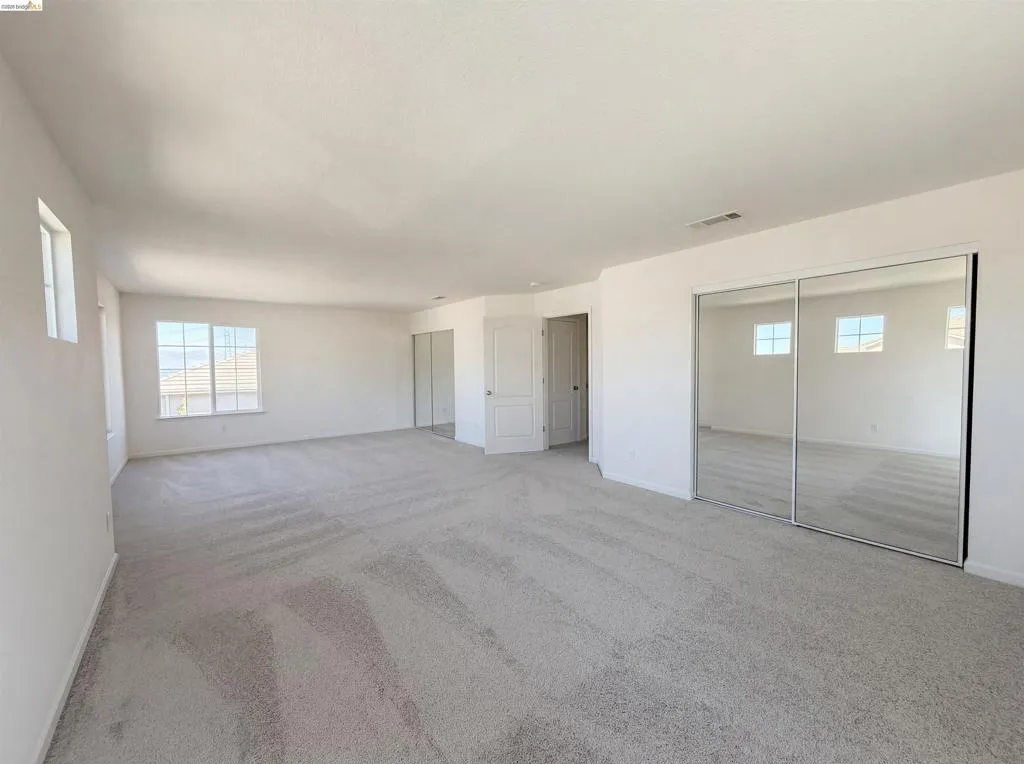 Unfurnished bedroom featuring light carpet, multiple windows, and two closets