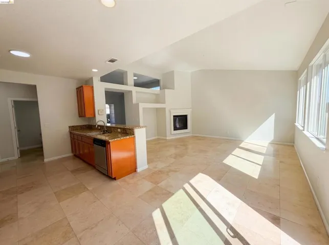 Kitchen featuring dark stone countertops, open floor plan, a glass covered fireplace, wood finish cabinets, and lofted ceiling