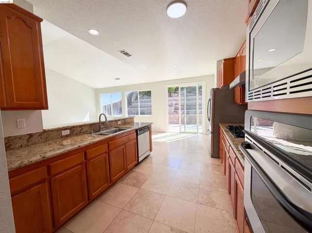 Kitchen featuring stainless steel appliances, wood finish cabinets, light stone countertops, recessed lighting, and light tile patterned flooring