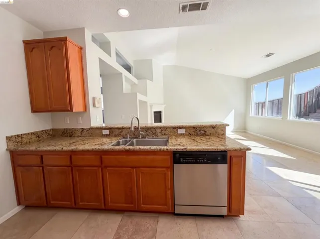 Kitchen with stainless steel dishwasher, wood finish cabinetry, light stone countertops, a peninsula, and open floor plan