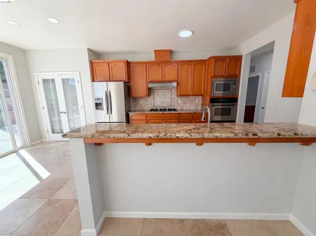 Kitchen with a breakfast bar area, light stone countertops, stainless steel appliances, a peninsula, and tasteful backsplash
