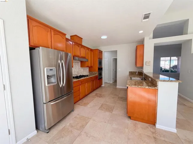 Kitchen with stainless steel appliances, a peninsula, light stone countertops, wood finish cabinets, and recessed lighting