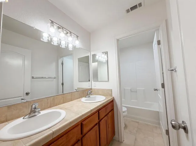 Bathroom featuring double vanity, shower / bathtub combination, and light tile patterned floors