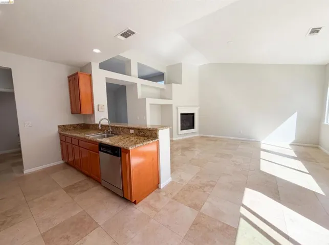 Kitchen with light stone counters, wood finish cabinetry, a glass covered fireplace, dishwasher, and vaulted ceiling