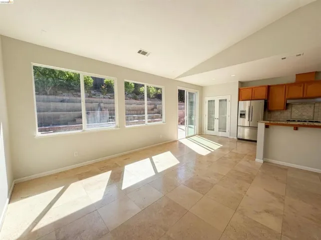 Kitchen featuring wood finish cabinets, stainless steel refrigerator with ice dispenser, vaulted ceiling, tasteful backsplash, and french doors