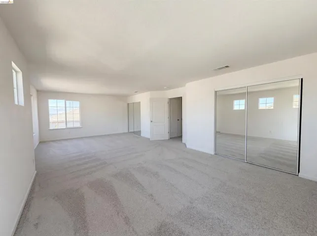Unfurnished bedroom featuring light carpet, multiple windows, and two closets