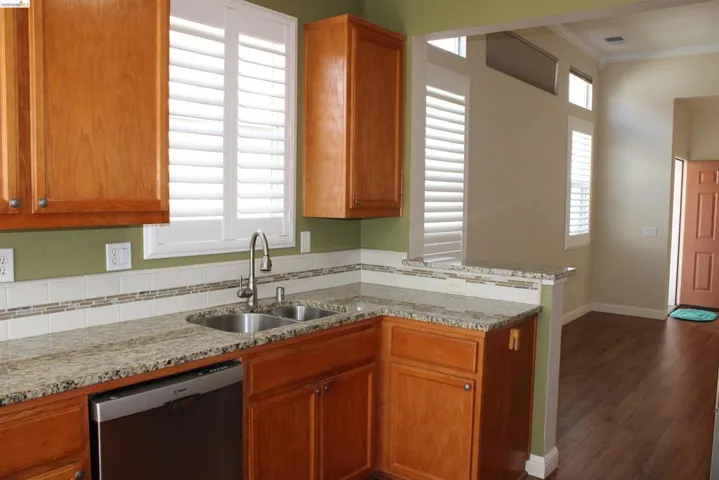 Kitchen with light stone counters, dishwasher, ornamental molding, wood finish cabinetry, and a peninsula