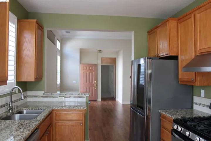 Kitchen with stainless steel gas range oven, wood finish cabinets, light stone countertops, and plenty of natural light
