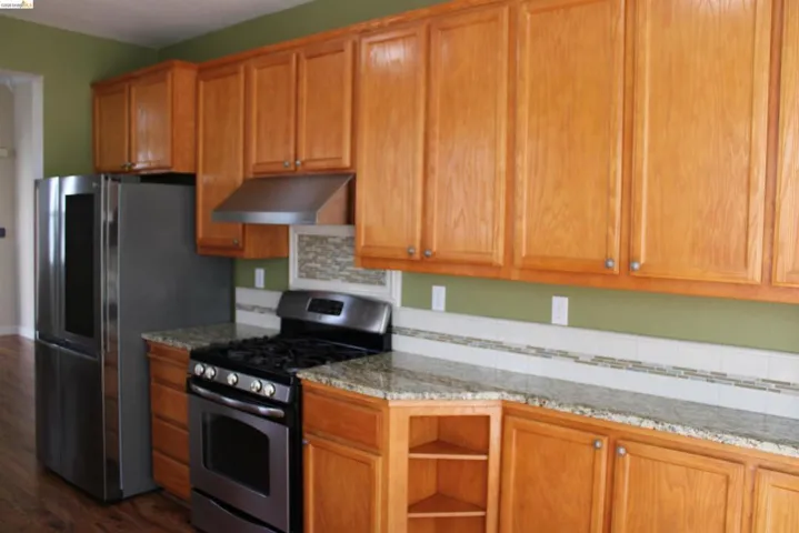 Kitchen with stainless steel gas stove, wood finish cabinetry, open shelves, and dark wood-type flooring