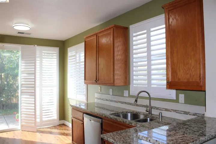 Kitchen with wood finish cabinetry, dishwasher, dark stone counters, and light wood-style floors