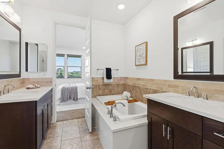 Ensuite bathroom featuring two vanities, a bath, light tile patterned floors, recessed lighting, and light colored carpet