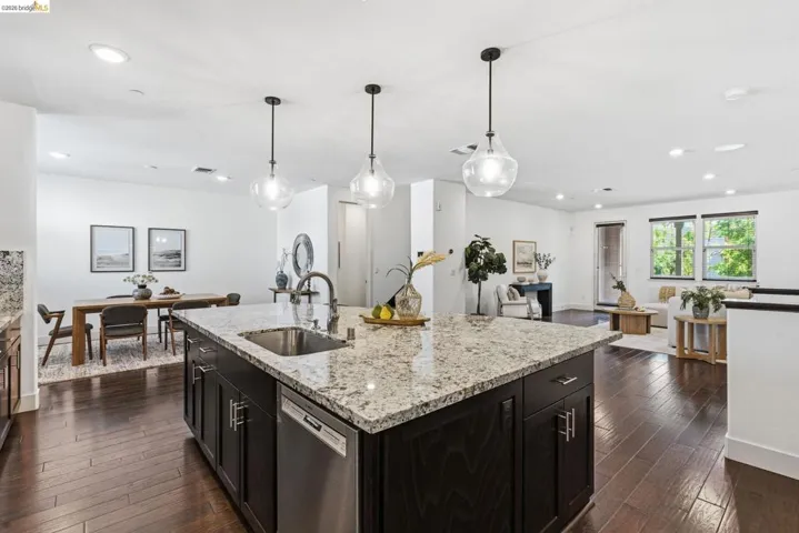 Kitchen with open floor plan, light stone counters, stainless steel dishwasher, and dark wood-style flooring