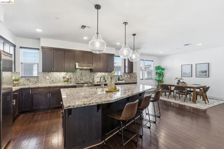 Kitchen featuring light stone countertops, dark wood finished floors, a breakfast bar, an island with sink, and dark wood finish cabinetry