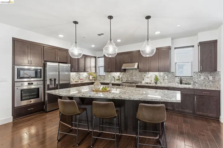 Kitchen with stainless steel appliances, a kitchen breakfast bar, light stone countertops, and dark wood finish cabinets
