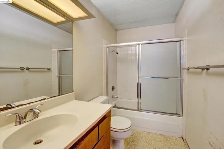 Full bathroom featuring vanity, combined bath / shower with glass door, and a textured ceiling