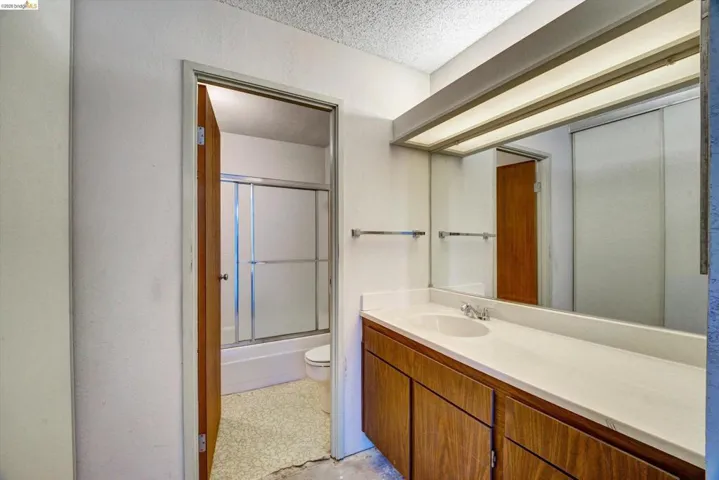 Bathroom featuring vanity, shower / bath combination with glass door, and a textured ceiling