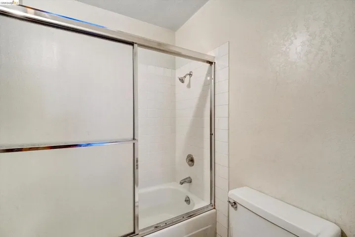 Full bath featuring bath / shower combo with glass door and a textured wall