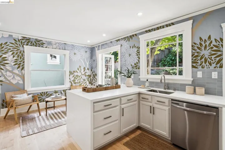 Kitchen featuring wallpapered walls, a peninsula, stainless steel dishwasher, white cabinetry, and light stone countertops