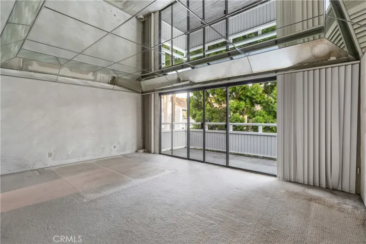 Primary bedroom with high ceilings, mirrored accents, and access to a private balcony.

