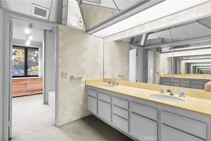 Spacious primary bathroom with dual-sink vanity, extensive cabinetry, and mirrored accents throughout.