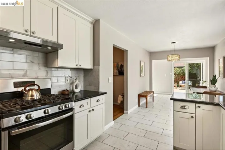 Kitchen with stainless steel range with gas stovetop, dark stone countertops, white cabinets, backsplash, and decorative light fixtures