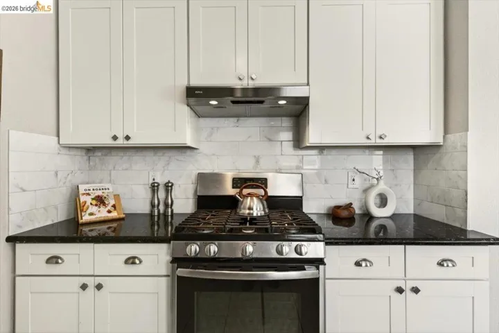 Kitchen with stainless steel gas stove, dark stone counters, and white cabinetry