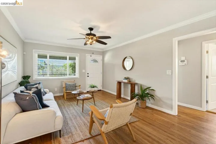Living area with a ceiling fan, light wood-type flooring, and crown molding
