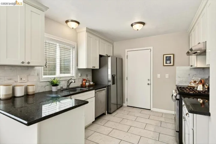 Kitchen with white cabinets, stainless steel appliances, tasteful backsplash, and dark stone countertops